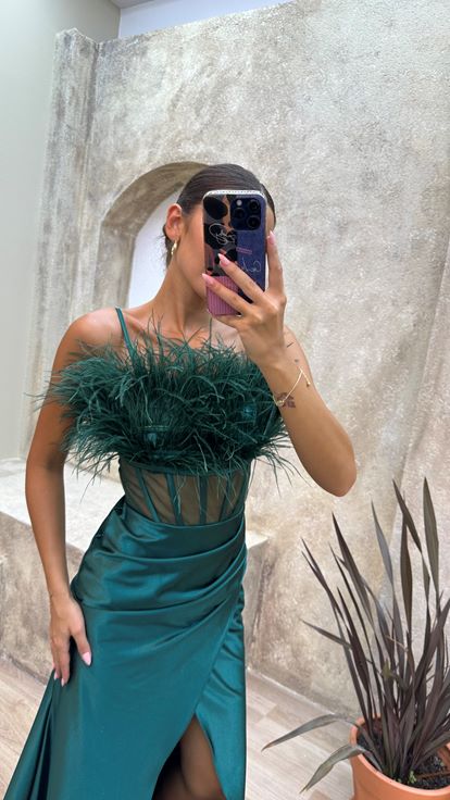 Vestido de noche de satén verde esmeralda con tirantes y detalle de plumas en el busto y la cintura 