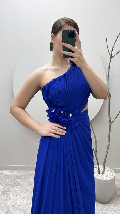 فستان سهرة من ساكس بمقاسات كبيرة بكتف واحد وتفاصيل وردة عند الخصر والكتف