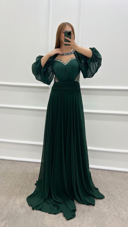 فستان أخضر زمردي بمقاسات كبيرة، صدر شفاف وأكمام واسعة، مزين بأحجار الراين 