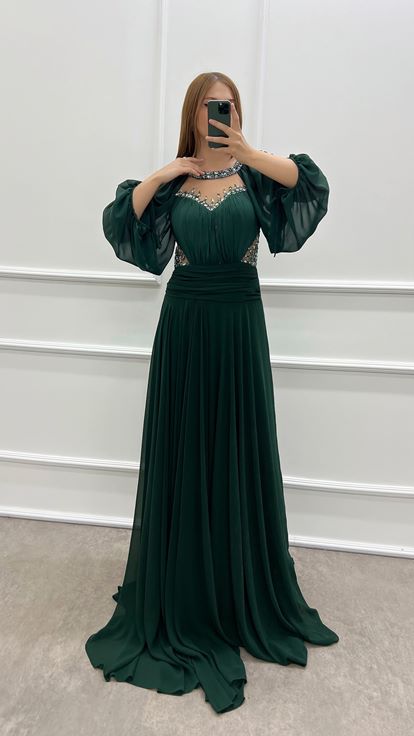 فستان أخضر زمردي بمقاسات كبيرة، صدر شفاف وأكمام واسعة، مزين بأحجار الراين 