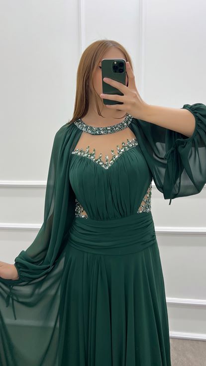 فستان أخضر زمردي بمقاسات كبيرة، صدر شفاف وأكمام واسعة، مزين بأحجار الراين 