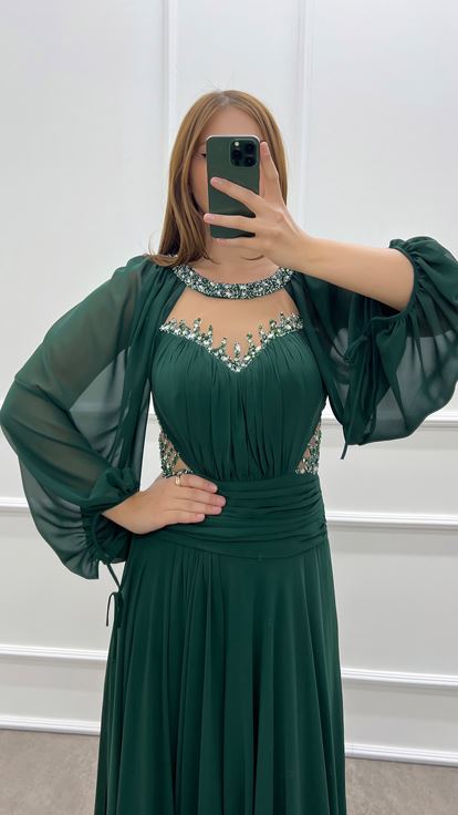 فستان أخضر زمردي بمقاسات كبيرة، صدر شفاف وأكمام واسعة، مزين بأحجار الراين 