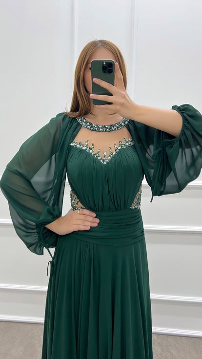 فستان أخضر زمردي بمقاسات كبيرة، صدر شفاف وأكمام واسعة، مزين بأحجار الراين 
