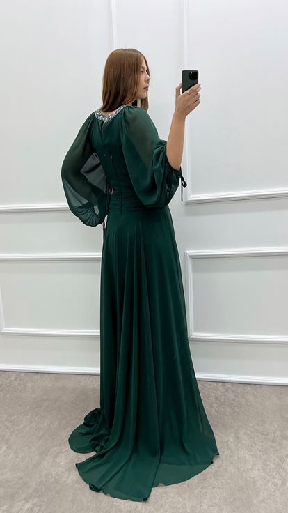 فستان أخضر زمردي بمقاسات كبيرة، صدر شفاف وأكمام واسعة، مزين بأحجار الراين 