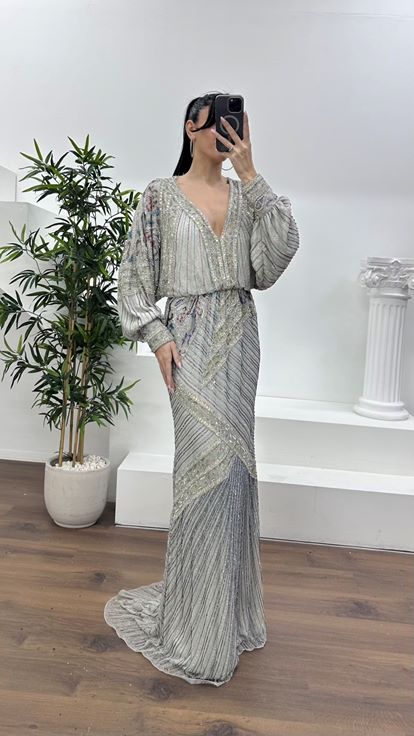 فستان سهرة فضي اللون بياقة على شكل حرف V عميقة وأكمام واسعة مزينة بكشكشة