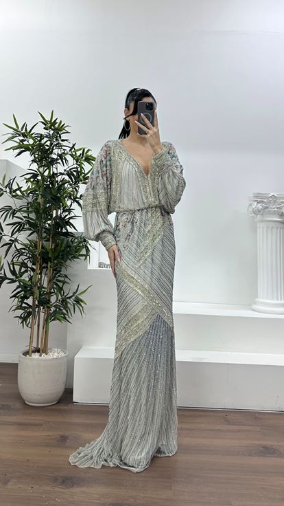 فستان سهرة فضي اللون بياقة على شكل حرف V عميقة وأكمام واسعة مزينة بكشكشة