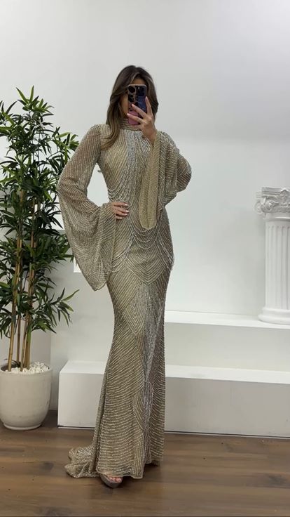 فستان سهرة كريمي اللون، بأكمام واسعة مزينة بتفاصيل دقيقة، وقصة متدلية مطرزة بالخرز 